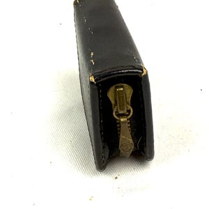 May include: A black leather wallet with a brass zipper. The rectangular wallet is closed, with the zipper pull at the bottom. The leather shows some wear and tear, with slight discoloration and scuff marks. The wallet is set against a white background.