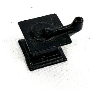 May include: A small, black cast iron stove with a handle on the side. The stove is about 3 inches tall and 2 inches wide.