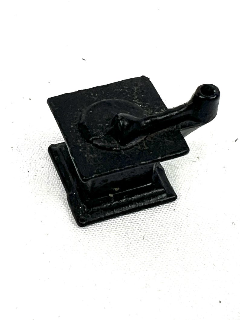 May include: A small, black cast iron stove with a handle on the side. The stove is about 3 inches tall and 2 inches wide.
