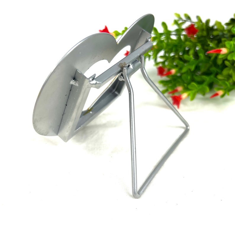May include: Silver metal easel stand with a heart-shaped top. The stand is designed to hold a small picture or photo.