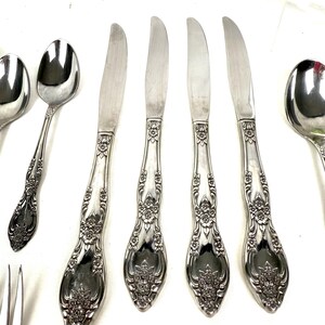 May include: Silverware set featuring ornate floral detailing on the handles. The set includes spoons, knives, and forks, all with a polished finish. The knives have a curved blade design.