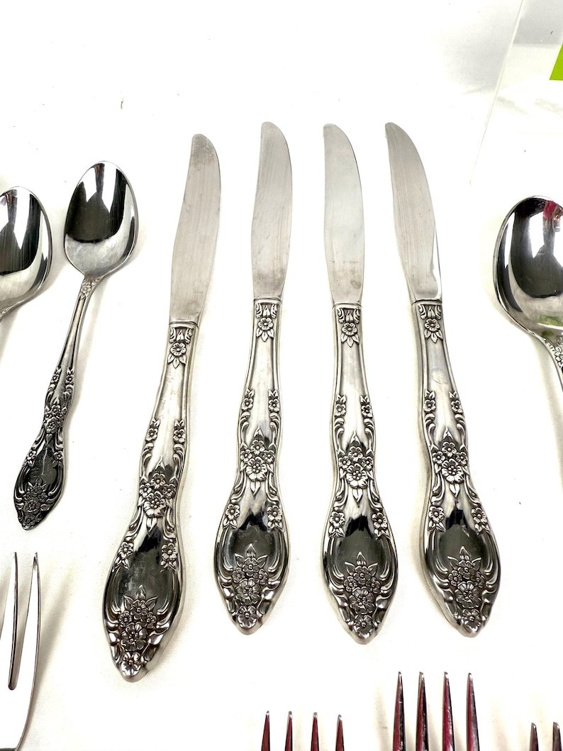 May include: Silverware set featuring ornate floral detailing on the handles. The set includes spoons, knives, and forks, all with a polished finish. The knives have a curved blade design.