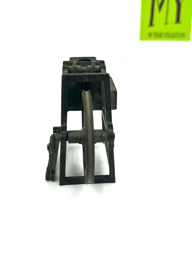 May include: A black metal toy model of a small industrial machine with a wheel and gears. The model is made of metal and has a realistic design.