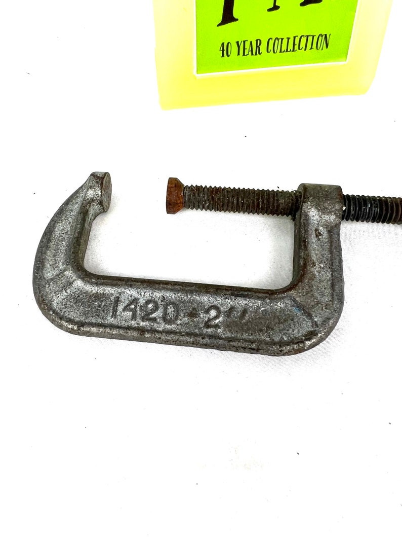 May include: A silver metal C-clamp with a threaded screw. The clamp has a 1420-2 marking on the side.