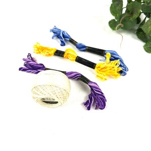 May include: A ball of white yarn with three skeins of embroidery floss in purple, yellow, and blue.