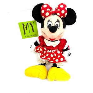 Vintage Minnie Mouse plush doll wearing a red polka dot dress and bow, displayed upright on a white background