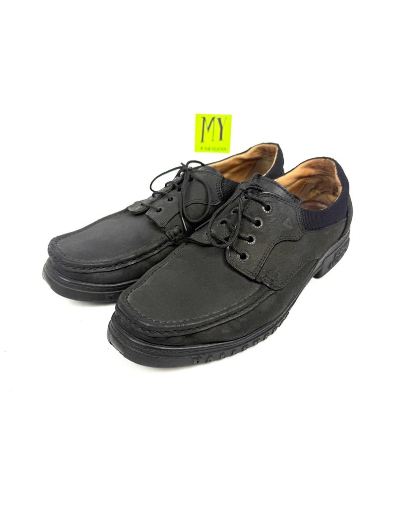 May include: Pair of black leather lace-up shoes. The shoes have a rounded toe, a thick sole, and a padded collar. The laces are black, and the interior is a light brown color. The shoes are displayed on a white background.