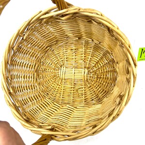 May include: A woven wicker basket with a single handle. The basket is light brown and has a round shape.