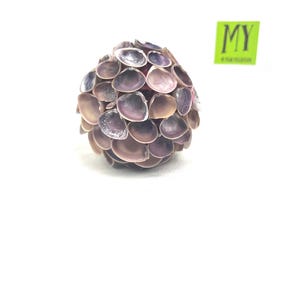 May include: A sphere made of many small, purple and brown seashells. The shells are arranged in a layered pattern, creating a textured surface.