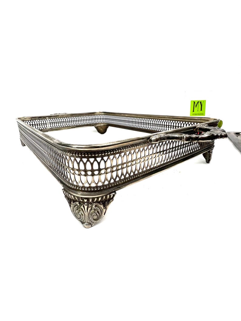 May include: Silver-plated serving tray with a decorative, openwork design and four ornate feet. The tray has a rectangular shape and a handle on one side.