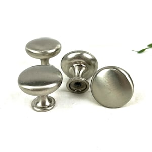 Może przedstawiać: Cztery srebrne gałki do szafek z okrągłym, lekko wypukłym wierzchołkiem i krótką, cylindryczną podstawą.