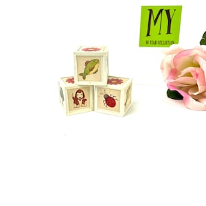 May include: Three wooden blocks with colorful illustrations of a fish, a ladybug, and a dog. The blocks are white with green trim and are stacked on top of each other.