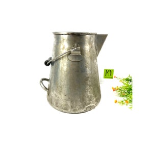 May include: A vintage aluminium camping coffee pot with a handle and a spout. The pot has a worn, aged look and is made of metal.