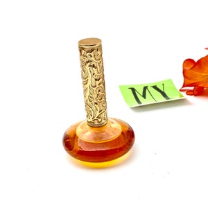May include: A vintage perfume bottle with a gold, ornate cap and a clear amber glass base. The bottle is sitting on a white surface.