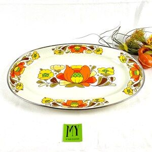 May include: A white oval serving platter with a brown, orange, and yellow floral design. The platter has a silver rim.