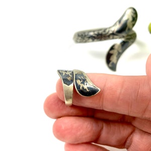 May include: A silver ring with a black and silver design. The ring is shaped like a snake and is wrapped around a finger.