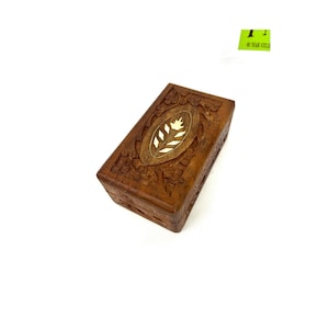 May include: A small, rectangular wooden box with intricate carvings. The box has a floral design with a white inlay in the center. The box is made of dark brown wood.