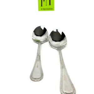 May include: Two silver serving spoons with a slotted design on the spoon head. The handles have a beaded edge and a rectangular design at the end. A green square with the text "MY" is in the background.