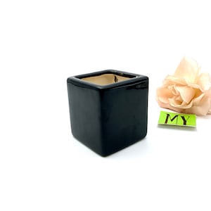 May include: A black square ceramic planter with a smooth, glossy finish. The planter is empty and ready for a small plant.