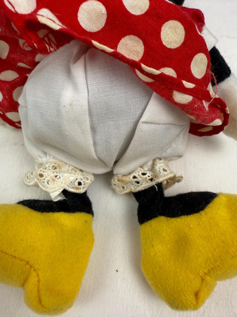 May include: A plush doll featuring a red and white polka dot dress, white bloomers with lace trim, and yellow shoes with black accents. The doll's design is reminiscent of a classic cartoon character.