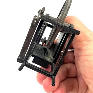 May include: A small, black metal pencil sharpener shaped like a spinning wheel. The sharpener has a small, round blade and a crank that turns the wheel.