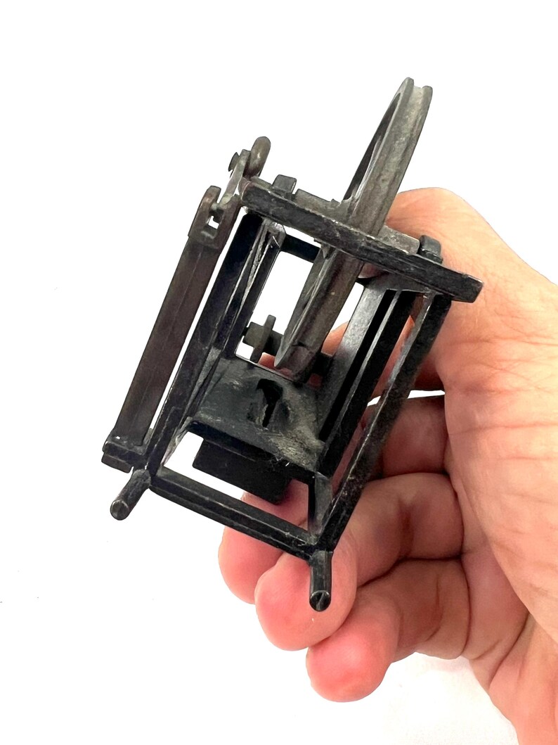 May include: A small, black metal pencil sharpener shaped like a spinning wheel. The sharpener has a small, round blade and a crank that turns the wheel.