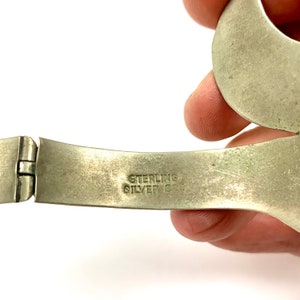 May include: Close-up of a silver bracelet with a hinged clasp. The bracelet is marked "STERLING SILVER 925".