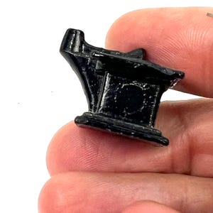 May include: A small, black metal anvil with a rounded top and a flat base. The anvil is approximately 5 cm tall and 2.5 cm wide.