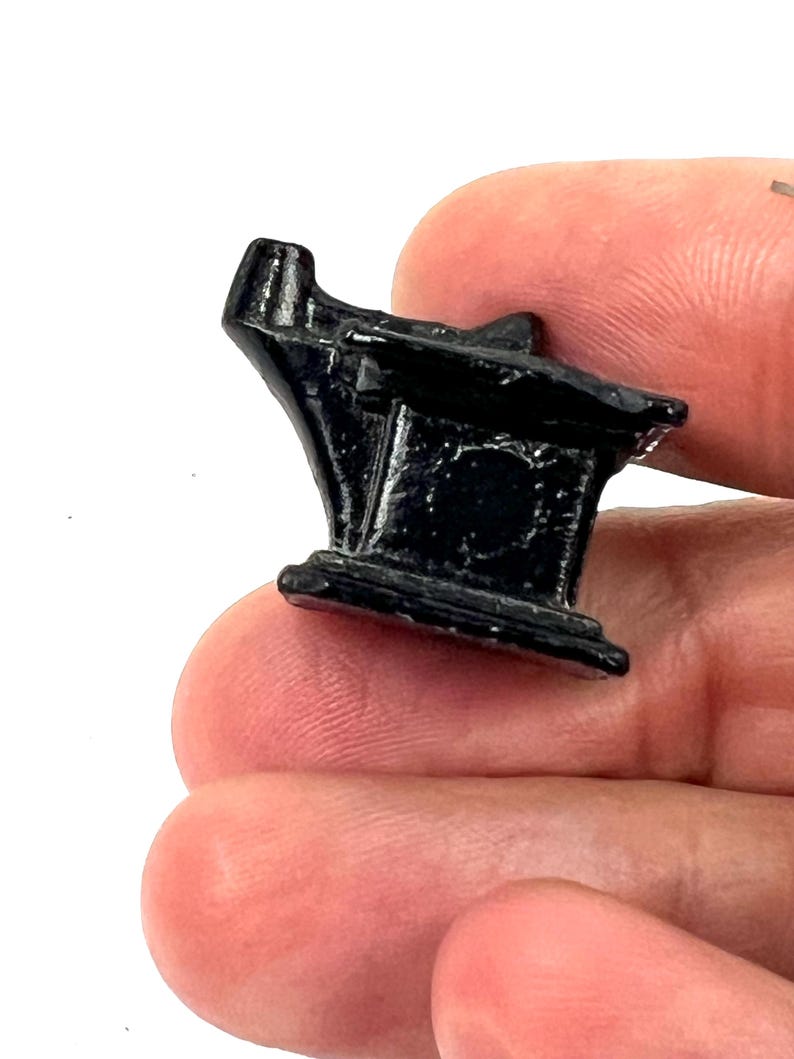 May include: A small, black metal anvil with a rounded top and a flat base. The anvil is about 2 inches tall and 1 inch wide.