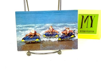 Postal fotográfica vintage de playa: Tres chicos surfeando, 1969