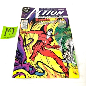 Peut inclure: Une couverture de bande dessinée représentant un super-héros rouge avec une cape et un 'D' sur la poitrine, volant dans les airs avec une créature démoniaque violette en arrière-plan. Le texte de la couverture indique "Action Comics Weekly" et "Deadman: The Demon Within".