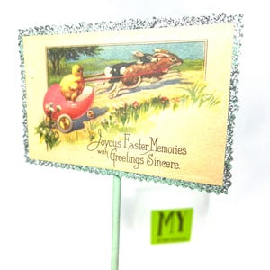 May include: Vintage Easter greeting card on a stick. The card features a chick in a red carriage pulled by two rabbits. The card has a glittery border and the text "Joyous Easter Memories with Greetings Sincere."