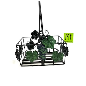 Op de afbeelding: Zwarte metalen draadmand met een handvat en een wijnstokontwerp. De mand heeft groene bladeren en paarse druiven. De mand is gelabeld met "MY HOME COLLECTION".