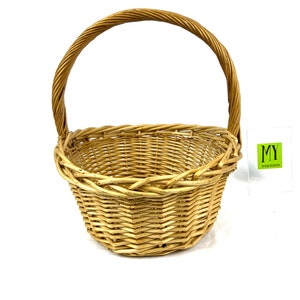 May include: A natural woven wicker basket with a single handle. The basket is light brown in color and has a rounded shape.