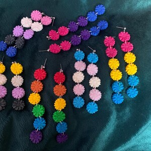 May include: Several pairs of dangle earrings featuring vertical arrangements of small, textured flower-shaped beads in various colours including pink, white, purple, black, blue, yellow, orange, green, and red, all attached to silver-toned earring posts.