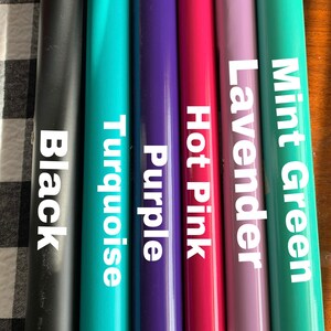 May include: A collection of vinyl rolls in various colors, including black, turquoise, purple, hot pink, lavender, and mint green. Each roll is labeled with its respective color name in white text.