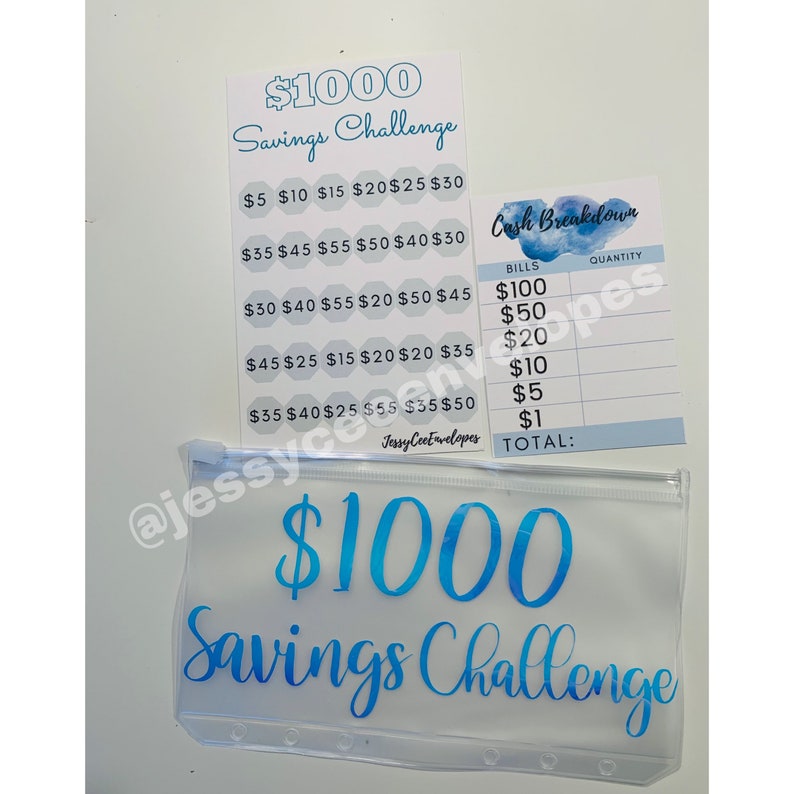 May include: A clear vinyl savings envelope and two matching cards with blue text. The envelope and one card read "$1000 Savings Challenge." The second card is a "Cash Breakdown" sheet for tracking bills.