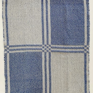May include: A rectangular textile piece featuring a woven pattern of large alternating blue and off-white squares. The design includes thin, double-line blue stripes that intersect to form a grid, creating a balanced, symmetrical check motif.