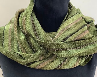 May include: A textured infinity scarf featuring a variegated pattern of olive green, sage, and dark brown stripes. The fabric has a looped, woven construction with a soft, dimensional surface that wraps around the neck in a continuous circle.