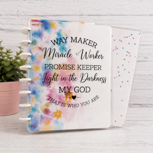 May include: A disc-bound notebook with a watercolor-style cover featuring blue, pink, and yellow hues. The text reads: WAY MAKER Miracle Worker PROMISE KEEPER Light in the Darkness MY GOD THAT IS WHO YOU ARE. It has white plastic discs and a clear cover.