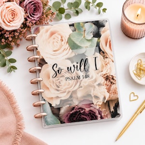 May include: A disc-bound planner featuring a floral cover with pink and mauve roses, eucalyptus leaves, and the text So will I PSALM 148. The planner has copper-colored discs and is surrounded by a candle, gold paper clips, and a gold pen.