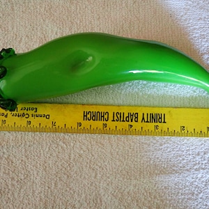 May include: A green glass vase shaped like a chili pepper. The vase is 12 inches long and has a ruffled opening.