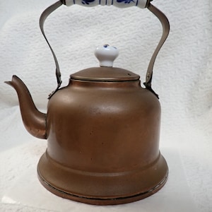 May include: A copper tea kettle with a white porcelain handle and knob. The handle has a blue and white floral design.