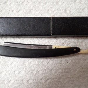 May include: A black and white straight razor with a bone handle and a black leather case.