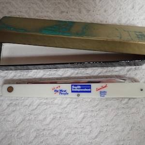 May include: White pocket knife with a silver blade and a blue and red logo that reads "We are the Meat People Swift Independent Commitment Quality Service Trust". The knife is in a black and gold box.