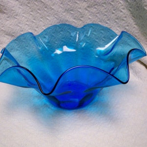 May include: A large, blue glass bowl with a wavy, ruffled rim. The bowl is made of clear glass and has a light blue tint.
