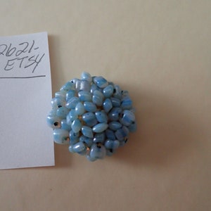 May include: A cluster of small, light blue and white, irregularly shaped, glass beads, arranged in a circular shape.