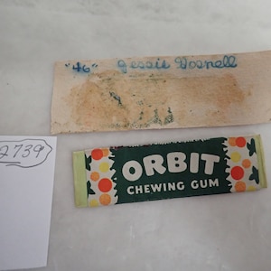 May include: An image featuring a pack of "Orbit Chewing Gum" with a green and white design, and a vintage label with the text "46" and "Jessie Dosnell" in blue ink. A white paper with the number "2739" is also visible.