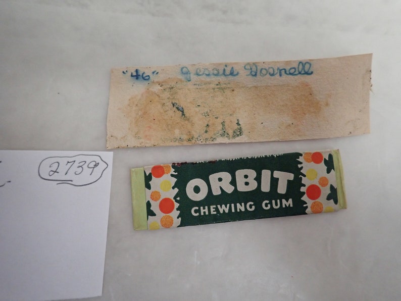May include: An image featuring a pack of "Orbit Chewing Gum" with a green and white design, and a vintage label with the text "46" and "Jessie Dosnell" in blue ink. A white paper with the number "2739" is also visible.