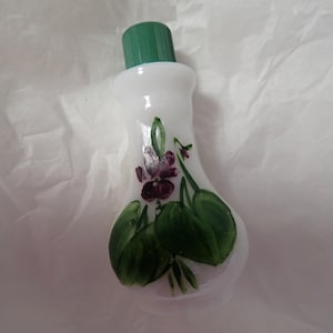 May include: White glass bottle with a green lid and a painted design of purple flowers and green leaves.